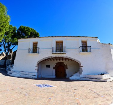 Panoramic front view of Ermita de la Magdalena among pine trees and its tiled main entrance on a sunny day. High-quality photo