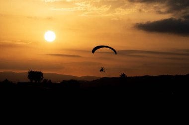 Paramotor trike silueti, sıcak bir turuncu yaz akşamında günbatımını arka plan olarak kullanıyor. Yüksek kaliteli fotoğraf.