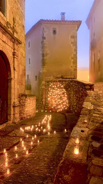 Bir ortaçağ köyündeki kaldırım taşı sokakta alacakaranlıkta yanan mumlarla aydınlatılarak büyülü bir atmosfer yaratıldı.