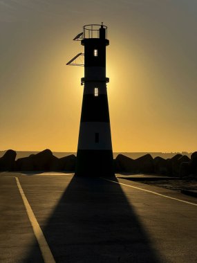 Gün batımında dalgakıranın sonundaki küçük bir deniz fenerinin siluetinin dikey görüntüsü. Yüksek kalite fotoğraf
