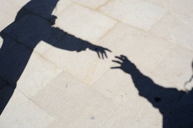Güneşli kaldırımda uzanan iki elin gölgeleri.