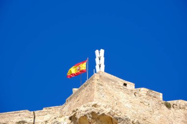 İspanya bayrağı açık mavi gökyüzüne karşı Santa Barbara kalesinde dalgalanıyor..