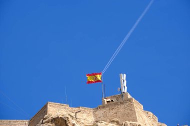 İspanyol bayrağı eski kalenin duvarında dalgalanırken berrak mavi gökyüzüne karşı tezatlarla.