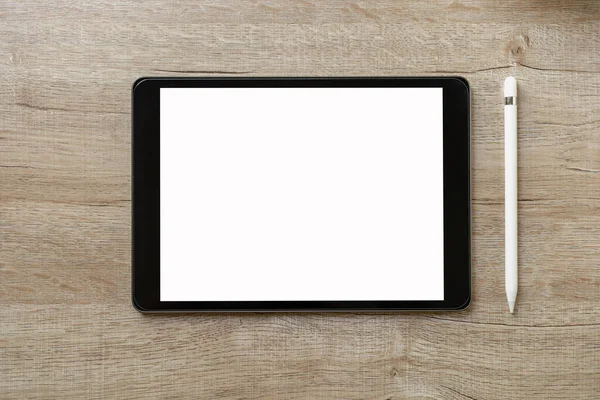 Black tablet with white blank screen is on top of brown paper with supplies. Top view, flat lay.