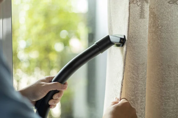 man dry cleaning curtain with vacuum cleaner. in living room at home.