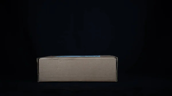 黒の背景に隔離されたストレスのかかる木のテーブルの上に垂直に提示クラフト段ボールパッケージボックス — ストック写真