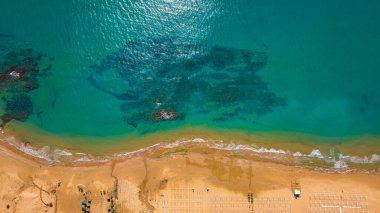 Havadan kumsal manzarası, yaz tatili şablonu afişi. Dalgalar inanılmaz mavi okyanuslarla, deniz kıyılarıyla, sahil şeridiyle sörf yapar. Mükemmel bir hava aracı üst görüntüsü. Huzurlu, parlak sahil, deniz kenarı.