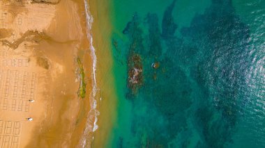 Havadan kumsal manzarası, yaz tatili şablonu afişi. Dalgalar inanılmaz mavi okyanuslarla, deniz kıyılarıyla, sahil şeridiyle sörf yapar. Mükemmel bir hava aracı üst görüntüsü. Huzurlu, parlak sahil, deniz kenarı.