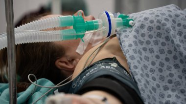 Tansiyon monitörü ve solunum cihazına bağlı olan kadın ameliyata hazırlanıyor. Ameliyat koltuğunda oturan kadın ameliyatın başlamasını bekliyor.