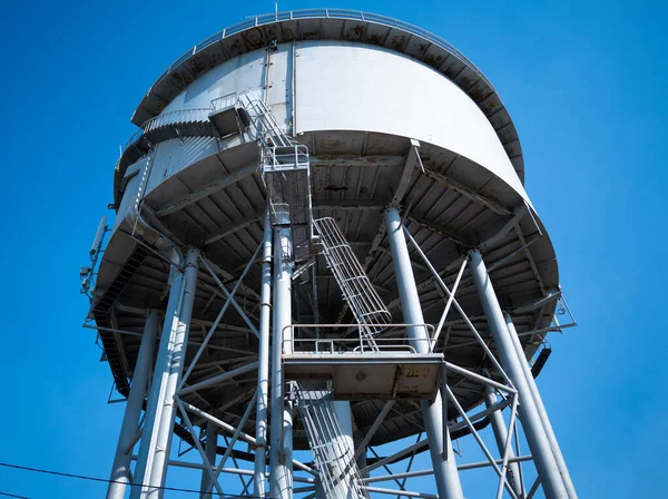 A low angled photograph of a grey colored water tower in Nightcliff, Darwin, showing the structural engineering informing the struts and bracing capable of supporting a full water tank.