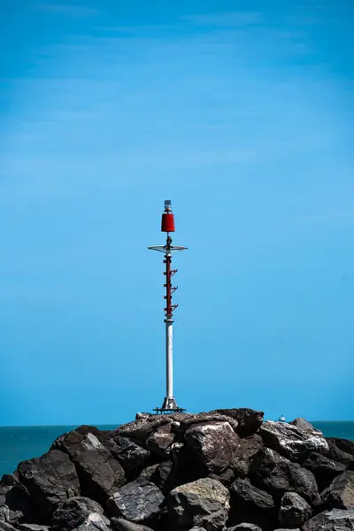一座红白相间的水上导航灯塔矗立在一堆岩石之上 与美丽的蓝天形成鲜明对比 — 图库照片
