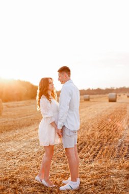 A Ukrainian couple walks through a field and looks into each other's eyes. Blue shirt and denim shorts. White short dress