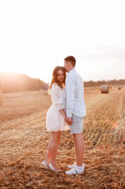 A couple in love walks at sunset in the middle of a wheat field. White clothes of husband and wife. Flag of Ukraine