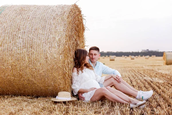 A pregnant wife and husband rest in a mowed wheat field on a picnic. Sunset