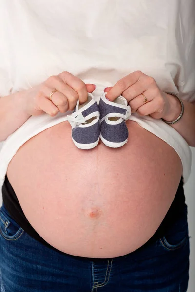 The expectant mother holds baby shoes on her stomach and waits for the baby to arrive. Childhood is the best time in life
