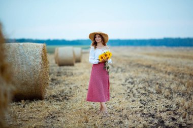 A girl in a hat walks through a wheat field