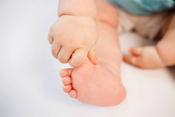 Мальчик держит свою маленькую ножку рукой