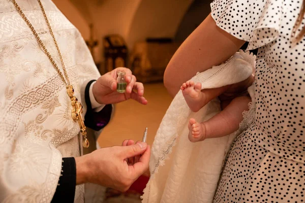 Small feet of a child in a dark Orthodox church during the Sacrament of Baptism. The priest is next to the parents