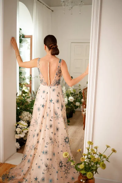 A girl in a long dress among flowers in a photo studio. Beautiful hairstyle and refined interior