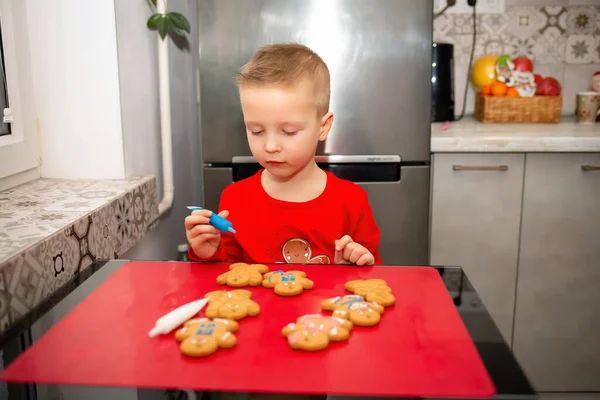 Christmas morning at home in Ukraine. Coloring cookies with blue paint. A red sweater on a boy and a red table