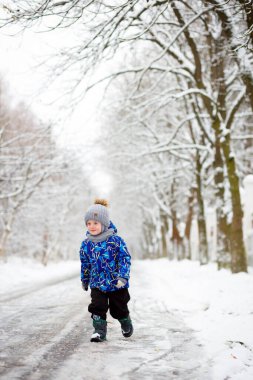 Kar fırtınasında, başında kartopu olan, kışın ormanda gülümseyen çocuk. Karlı Kışın Komik Çocuğu