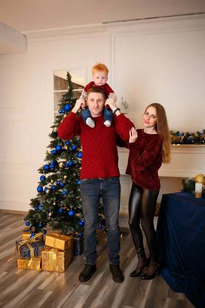 Mom, son and dad together near the Christmas tree with toys and gifts for the coming year 2023. Year of the Rabbit. Burgundy sweaters on all family members