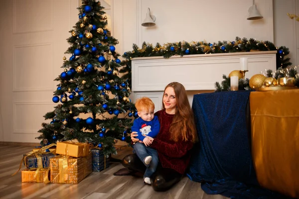 Mother and son at Christmas near the Christmas tree. Burgundy, blue and green colors for the New Year 2023