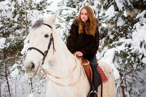 Winter coniferous forest with snow. A young girl with long hair in a fur coat riding a horse. Christmas atmosphere and holidays