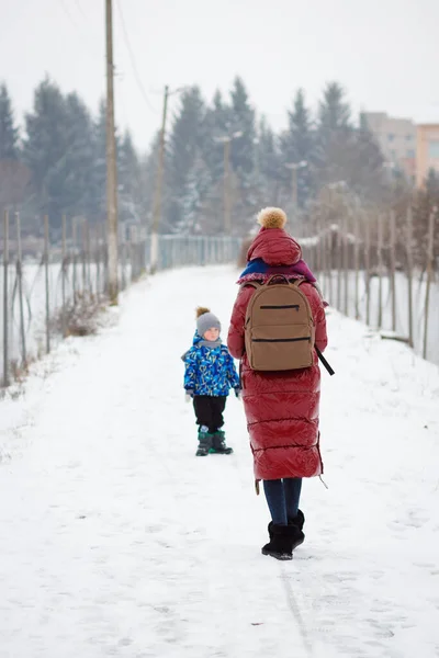 A mother walks with her son in the park. On the back is a large brown briefcase with a laptop and a phone for work