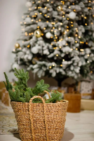 Sprigs of a Christmas tree in a wicker basket on the background of a Christmas tree with toys