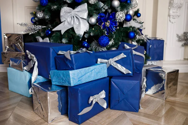 Decorated Christmas tree with blue toys and bows at home near the fireplace. Wrapped gifts for children