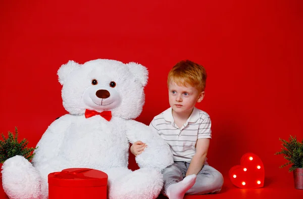 A red-haired boy with a white bear on a red background. Childhood in Ukraine. Russia started a war and all children are afraid of the sound of explosions