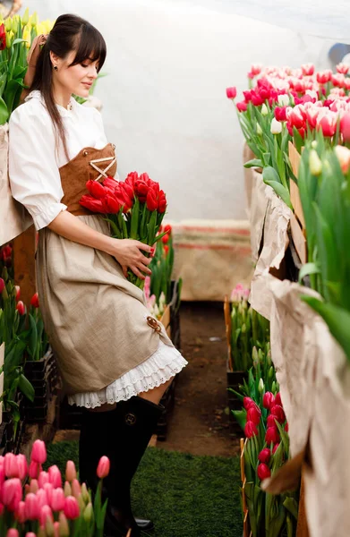 Camera tracking around pretty girl in sunhat sitting in pose in red tulip field