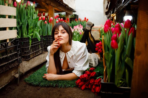 A gardener in a home greenhouse with tulips. Black boots. Green grass. Sexy girl