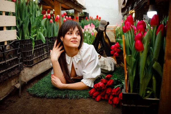A gardener in a home greenhouse with tulips. Black boots. Green grass