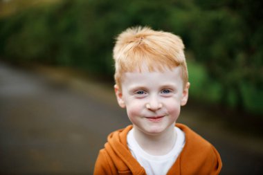 Gülümseyen kızıl saçlı bir çocuğun portresi. Mavi gözler ve şık bir takım elbise.