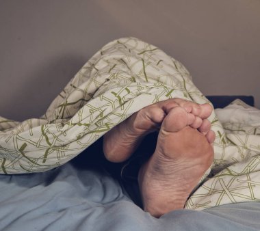 Adam battaniyenin altında yalınayak yatıyor.