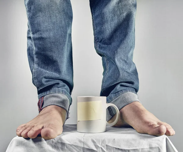 Male feet on white coffee cup with yellow sticky note