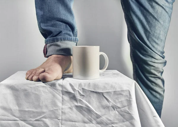 Male foot beside white coffee cup