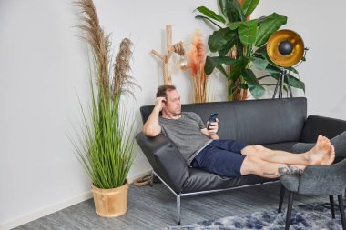 Oturma odasında çıplak ayakla kanepede oturan adam.