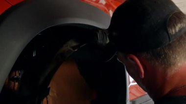 Otomobil tamircisi arabanın ön kemerleri için plastik aralıkları söker. Araba tamircisi arabanın ön kemerini söker. Son aşamada, kauçuk uzay araçları 4k kemerinden çıkartılır.