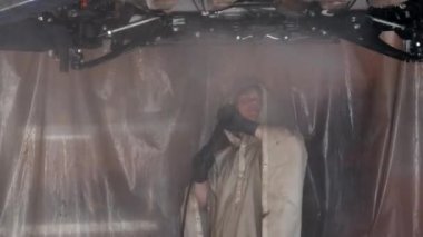 Yetişkin bir adam arabanın altını ve motorun koruyucu unsurlarını yıkıyor. Bir garaj işçisi, yüksek basınç altındaki bir silahtan çıkan su ile krank kutusunu ve motor korumasını yıkıyor. 4k