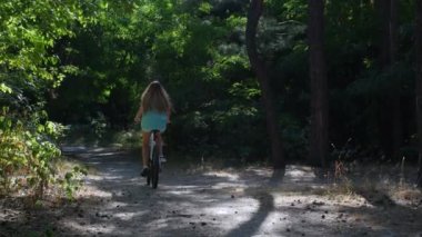 Şehir yeşil kozalaklı parkında heyecanlı bir bisiklet gezisi. Kız ormanda at biniyor. Yüksek kalite 4k görüntü