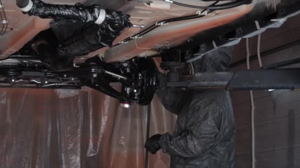 高质量的喷涂防腐蚀液体的工作由一个主人 汽车在起重机上 气缸上的工人用气枪操纵汽车 高质量的4K镜头 — 图库视频影像
