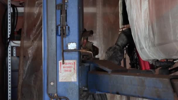 汽车在电梯上 工作台工作人员穿着工作服和面罩 在汽车轮拱上喷涂防腐蚀蜡材料 金属部件的保护 高质量的4K镜头 — 图库视频影像