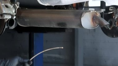 Anti-korozyon sıvısı püskürtmek için hortumları kontrol ediyorum. Asansördeki bir arabanın arka planında, bir araba tamircisi, korozyon önleyici maddeleri vücuda sıkmak için cihazı kontrol eder.