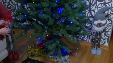 Yeni yıl için noel ağacının altında cücelerin kurulması. Noel için gri ve kırmızı renkli dekoratif Noel cüceleri ışıklarla parlayan bir ağacın altında. Yüksek kalite 4k görüntü