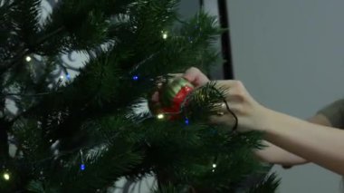 Güzel, uzun saçlı kız yılbaşı ağacını süslüyor. Güzel genç bir kadın evdeki Noel ağacına Noel süsleri asıyor ve gülümsüyor, çok mutlu. Yüksek kalite 4k görüntü