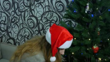 Güzel bir kadın yapay bir Noel ağacına asmak için oyuncak seçer. Uzun saçlı, kırmızı şapkalı güzel bir kadın camdan bir Noel oyuncağı tutuyor ve bir Noel 'e asıyor.