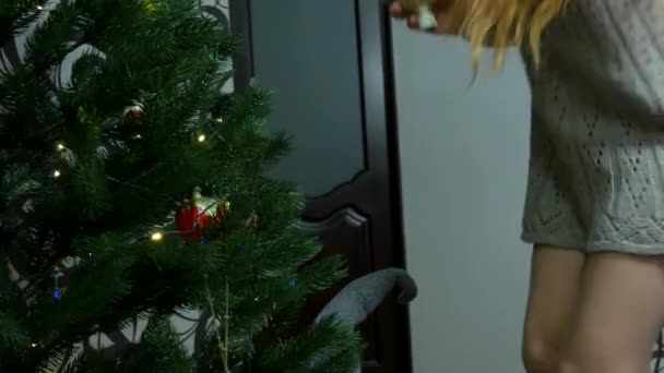 一个女孩把顶盖放在一棵新年树上 圣诞节假期 在家里 一个女人装饰着一棵人造的绿色圣诞树 为新年假期和新年做准备 高质量的4K镜头 — 图库视频影像